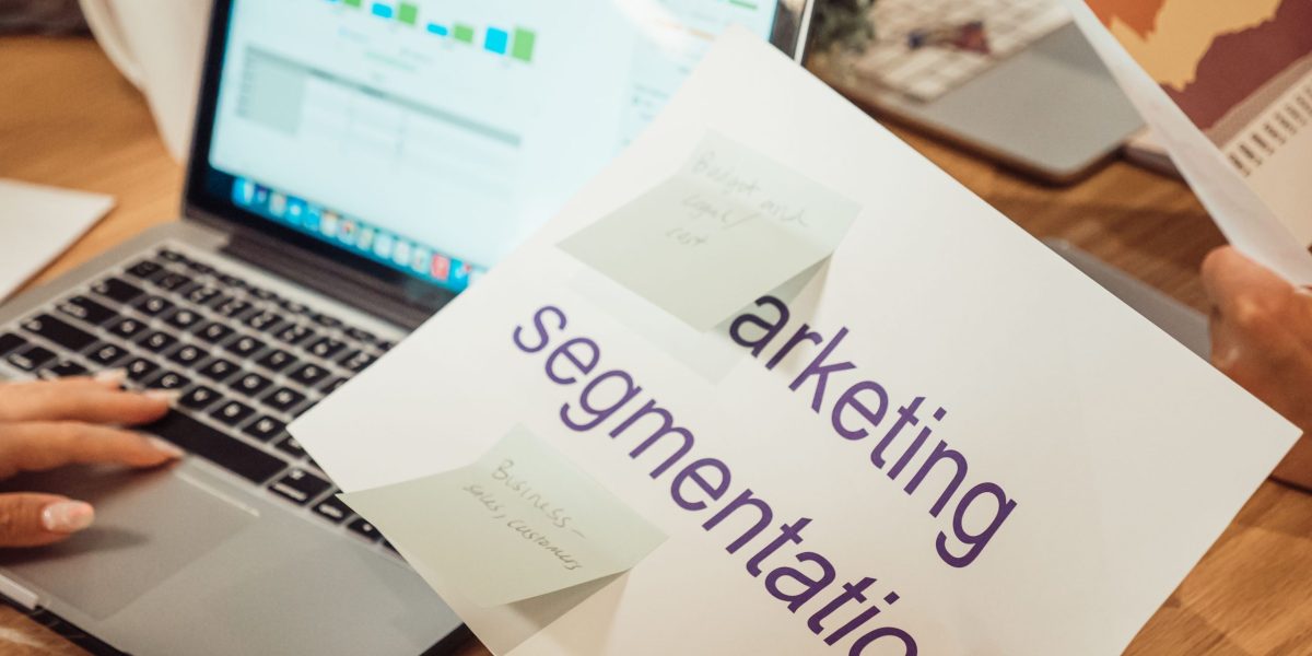 A modern workspace showing hands analyzing marketing data on a laptop and paper documents.